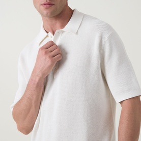 Model wearing Calvin Klein Jeans Waffle-Knit Logo Polo Shirt in Tofu, showing textured knit fabric and open polo collar detail.