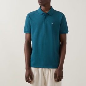 Model wearing Calvin Klein Jeans Tahoe Green Regular Polo, short sleeves, ribbed collar, small logo embroidery, styled with cream trousers