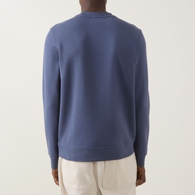 Model wearing Calvin Klein Jeans Badge Logo Sweatshirt in Blue Nomad, crew neck, ribbed hem, back view, styled with cream trousers