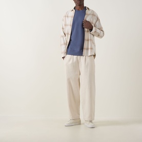 Model wearing Calvin Klein Jeans Badge Logo Sweatshirt in Blue Nomad, styled with pink plaid overshirt and cream wide-leg trousers.