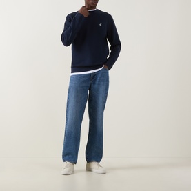 Model wearing Calvin Klein Jeans Monogram Logo Sweatshirt in black, crew neck with ribbed trims, styled with blue jeans and white trainers