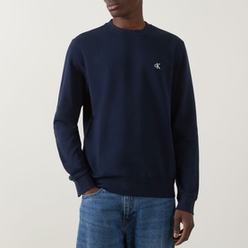 Model wearing Calvin Klein Jeans Monogram Logo Sweatshirt in black, crew neck with ribbed trims and embroidered logo, styled with blue jeans