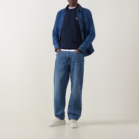 Model wearing Calvin Klein Jeans Monogram Logo Sweatshirt in black, styled with a denim overshirt and mid-blue relaxed-fit jeans.