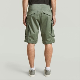 Model wearing G-Star cargo shorts in light sage green with large flap pockets, styled with a black tee and white trainers, rear view.