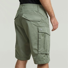 Model wearing G-Star cargo shorts in light olive green, featuring large side pockets and belt loops, shown from rear three-quarter angle.