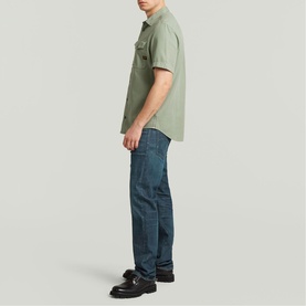 Model wearing G-Star Slim Shirt in light sage green with short sleeves and chest pockets, styled with dark indigo jeans and black loafers