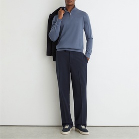 Model wearing Reiss airforce blue half-zip knit top with navy trousers and dark trainers, black jacket draped over shoulder