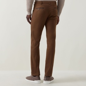 Model wearing Meyer brown cotton slim-fit chinos with rear welt pocket, styled with a cream knit and grey trainers.
