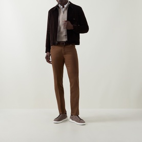 Model wearing Meyer brown cotton trousers styled with dark jacket, light shirt and grey slip-on trainers