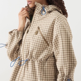 Model wearing Damson Madder Matilda Waterproof Gingham Raincoat in brown check with blue toggle drawstring waist detail and zip chest pocket.