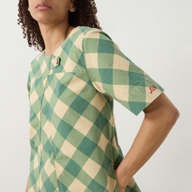 Model wearing Damson Madder Bridget Reversible Mini Dress in green and cream gingham, short sleeves, buttoned tab detail and embroidered logo