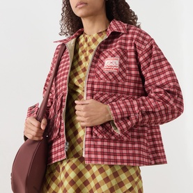 Model wearing Damson Madder Marcelle Reversible Barn Jacket in red multi check, styled with matching check dress and brown shoulder bag.