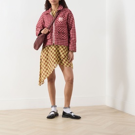 Model wearing Damson Madder Marcelle Reversible Barn Jacket in red multi gingham, styled with mustard check skirt and black loafers, carrying