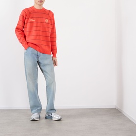 Model wearing Pellador Stripe Logo Sweater in red with crew neck, stripe pattern and logo detail, styled with light-wash jeans and silver trainers.