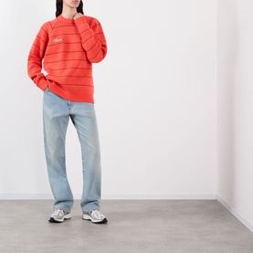 Model wearing Pellador Stripe Logo Sweater in red with crew neck, styled with light-wash straight-leg jeans and grey trainers