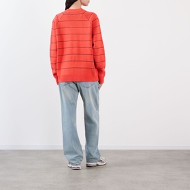 Model wearing Pellador Stripe Logo Sweater in red with crew neck and stripe pattern, styled with light blue wide-leg jeans and grey trainers.