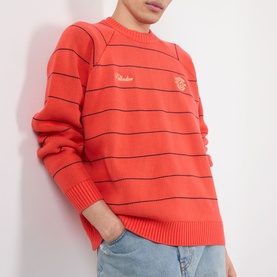 Model wearing Pellador Stripe Logo Sweater in red with black horizontal stripes, crew neck, embroidered script logo, paired with light blue jeans.