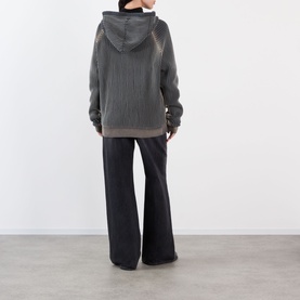 Model wearing Pellador Rib Knit Hoodie in grey, rear view, styled with wide-leg black trousers. Ribbed texture and dropped hem visible.