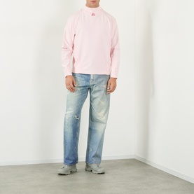 Model wearing Pellador Logo Mesh Football Training Top in pink with high ribbed neckline, styled with light wash distressed jeans and grey trainers.