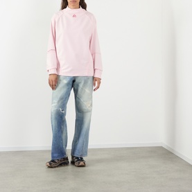 Model wearing Pellador Logo Mesh Football Training Top in pink with high ribbed neckline, styled with light wash distressed wide-leg jeans.