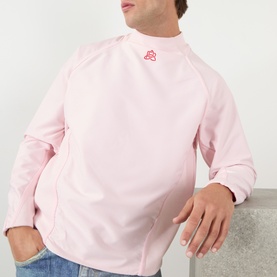 Model wearing Pellador Logo Mesh Football Training Top in pink, featuring high ribbed neckline, long sleeves, and red embroidered logo detail.
