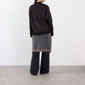 Model wearing Pellador Logo Football Training Sweatshirt in black, shown from behind, styled with grey layered skirt and wide-leg trousers.