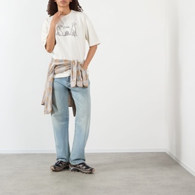 Model wearing Pellador Dog Tail Knot Logo T-Shirt in white with light-wash straight-leg jeans and a shirt tied at the waist.