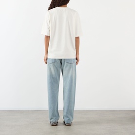 Model wearing Pellador Dog Tail Knot Logo T-Shirt in white, back view, with light wash wide-leg jeans.