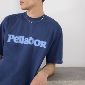 Model wearing Pellador Roundstone Logo T-Shirt in navy, featuring chest logo print, with a silver chain necklace.