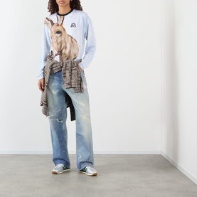 Model wearing Pellador Donkey Paint Graphic Long-Sleeved T-Shirt in white with donkey print, styled with distressed wide-leg jeans and a tied shirt.