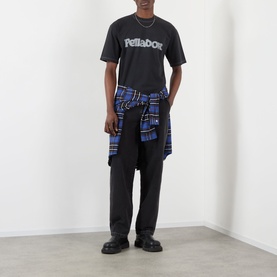 Model wearing Pellador Logo Print T-Shirt in black, styled with blue tartan shirt tied at waist and black trousers.