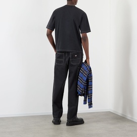 Model wearing Pellador Logo Print T-Shirt in black with black jeans, shown from behind, carrying a blue plaid shirt.