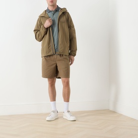 Model wearing Barbour clay casual jacket with grey polo shirt, khaki shorts and white trainers
