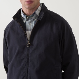 Model wearing Barbour navy casual jacket with zip fastening and funnel collar, styled with grey check shirt visible at neckline.
