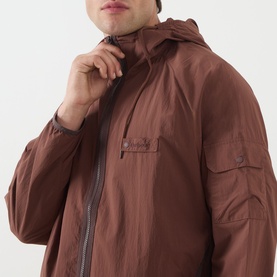 Model wearing Barbour Re-Engineered Flyweight Showerproof Jacket in Pepper, showing hood with drawstring and front zip fastening detail