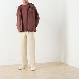 Model wearing Barbour Re-Engineered Flyweight Showerproof Jacket in Pepper, styled with cream trousers and white trainers.