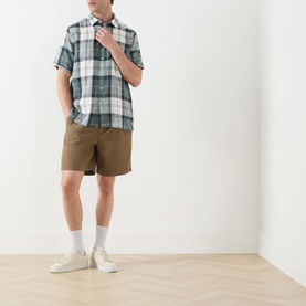 Model wearing Barbour casual shirt in Meadow Brook Tartan, short-sleeved check linen blend, styled with tan shorts and white trainers.