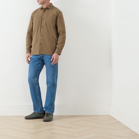 Model wearing a tan long-sleeve overshirt, styled with blue straight-leg jeans and grey slip-on shoes