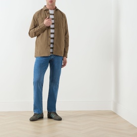 Model wearing tan overshirt jacket with grey striped T-shirt, blue straight-leg jeans and grey trainers