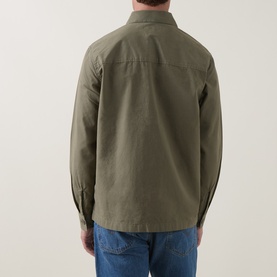 Model wearing Barbour casual shirt in Dusty Olive, rear view, relaxed fit cotton with long sleeves, styled with blue jeans.