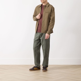 Model wearing Barbour Strick Flap Pocket Overshirt in Clay, styled with burgundy tee, olive trousers and brown trainers.