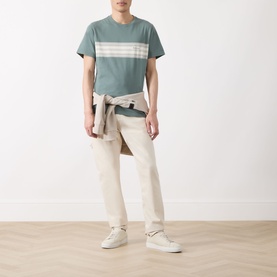 Model wearing Barbour Brayworth Graphic Logo T-Shirt in Vintage Teal with contrast chest stripes, styled with cream trousers and shirt tied at waist.