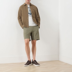Model wearing Barbour Harbourside Graphic T-Shirt in Whisper White with khaki shorts, brown overshirt, and dark trainers.