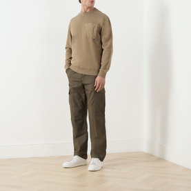 Model wearing Barbour Clay cotton crew neck sweatshirt with chest pocket, styled with dark olive cargo trousers and white trainers.