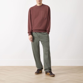 Model wearing Barbour Ivergill Patch Pocket Sweatshirt in Burnt Pepper, styled with olive straight-leg trousers and brown trainers.