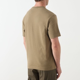 Model wearing Barbour Milburn Graphic Logo T-Shirt in Clay, back view, crew neck, short sleeves, styled with dark olive trousers