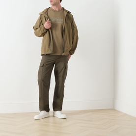 Model wearing Barbour Milburn Graphic Logo T-Shirt in Clay, styled with khaki zip-up hoodie, dark olive cargo trousers and white trainers.