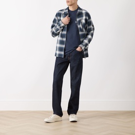 Model wearing Barbour Camping Trip T-Shirt in Navy, styled with blue plaid overshirt, dark jeans and white trainers.