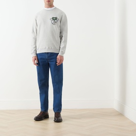 Model wearing Barbour Grey Marl cotton crew neck sweatshirt with small chest graphic, styled with blue jeans and brown boots.