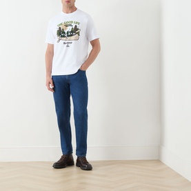 Model wearing white Barbour graphic T-shirt with green motif, styled with mid-blue straight-leg jeans and dark brown chunky shoes